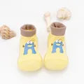 Close-up view of yellow breathable baby sock shoes with a blue cartoon character - Yellow Cartoon Letter A