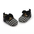 Nahaufnahme von Baby-Prinzessin-Schuhen mit schwarz-weißem Hahnentrittmuster und Schleife - Schwarz