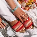 Nahaufnahme von flachen Boho-Sandalen mit lebhaften orange-roten Quasten und Webdetails - Rot