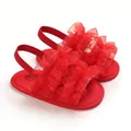 Detalle de sandalias rojas para bebé con suelas blandas y adornos de tul con volantes. - Rojo