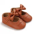 Detail von braunen Baby-Prinzessinenschuhen aus Leder mit großer Schleife und Wellenrand. - Braun