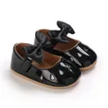 Gros plan de chaussures bébé fille en cuir verni noir avec nœud et détails pailletés. - Noir