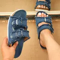 Dettaglio ravvicinato di sandali piatti in denim blu con doppie fibbie e bordi sfrangiati - Blu jeans
