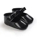 Detail view of shiny black patent leather baby girl Mary Jane shoes featuring a bow. - Black
