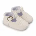 Nahaufnahme von cremefarbenen Babyschuhen mit Webstruktur und metallischem Schnallenverschluss. - Weiß