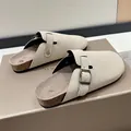 Detailed view of beige suede clogs featuring an adjustable buckle strap on a shoe box - Off White