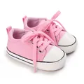 Nahaufnahme von rosa Baby-Leinwandschuhen mit weichen weißen Gummisohlen für Babys. - Rosa