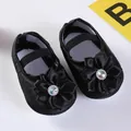 Nahaufnahme der schwarzen Baby-Prinzessinenschuhe aus Satin mit Schleifenblume und Strass - Strassblume Schwarz (GZ809)