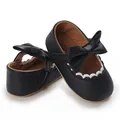 Close-up of black baby girl walking shoes featuring a large bow and white scalloped trim - Black