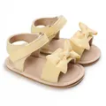 Detailed macro view of yellow baby sandals featuring a large bow and polka-dot straps - Yellow