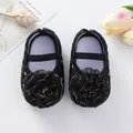 Vue détaillée de chaussures de princesse bébé noires avec fleurs en tissu à bord doré. - Noir