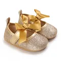 Close-up of gold glitter baby princess shoes with a large satin bow detail. - Gold