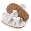 Detail view of white baby sandals featuring a soft rubber sole and elegant decorative bow - White