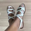 Detailed view of white flat sandals featuring cross-strap design and gold stud accents - White