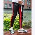 Detailed view of men's black track pants featuring red side stripes and ankle zipper design - Black and Red