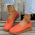 Gros plan de mocassins pour femmes orange vif avec coutures contrastées sur bois. - Orange