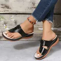 Detail view of black wedge flip-flop sandals worn with jeans in a rustic setting. - 35 / Black