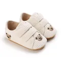 Gros plan de baskets bébé en velours côtelé blanc cassé avec broderie ours et velcro - Blanc