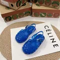 Primo piano di sandali jelly intrecciati blu traslucidi per bambini su un tappetino - Blu