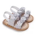 Primer plano de sandalias para bebé niña con lunares blancos y lazos decorativos. - Blanco