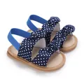 Primer plano de sandalias para bebé azul marino con lunares blancos y un lazo decorativo - Azul marino