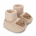 Primer plano detallado de los patucos beige para bebés con un tierno diseño de osito. - Amarillo claro