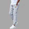 Close-up view of men's grey casual joggers featuring a stylish brown leather patch detail. - S / Gray