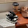 Primer plano de zapatillas infantiles en blanco y negro con velcro en mesa de madera - Talla 16 / Negro