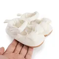 Gros plan sur des chaussures de marche pour bébé crème avec un grand nœud en dentelle. - Blanc