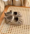 Gros plan de chaussures vintage en cuir beige pour bébé fille avec bout plissé et boucle - Kaki