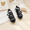 Schwarze Kinder-Sportsandalen mit drei Klettverschlüssen auf einem hellen Holztisch - 19.0 / Schwarz
