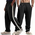 Gedetailleerde close-up van zwarte heren joggingbroek met sportieve zijstrepen en losse pasvorm. - Zwart