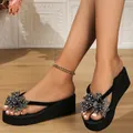 Primer plano de elegantes chanclas negras con cuña y un lazo de mariposa con pedrería - Negro - Flor Plateada