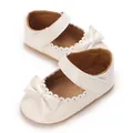 Close-up of white patent leather baby princess shoes with bow and scallop details - White