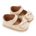 Close-up of beige baby Mary Jane shoes featuring a cute patent bow and scalloped trim. - Apricot