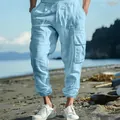 Close-up of light blue linen cargo joggers with drawstring and side pockets on a beach - S / Bottoms / Light Blue