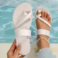 Close-up view of white toe-ring flat sandals being held over a blue pool background. - White