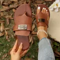Nahaufnahme von braunen flachen Zehentrenner-Sandalen mit dekorativer Metallplatte - Dunkelbraun
