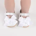 A close-up detailed view of white satin baby walking shoes with a large decorative bow - Insole Length 11cm / White