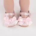 Macro view of pink satin baby walking shoes featuring large decorative bows for infants - Pink