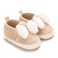 Detailed close-up view of beige fleece baby crib shoes with fluffy white faux fur bows - Apricot