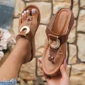Detalle de sandalias de cuña marrones con elegante adorno de hebilla metálica dorada. - Marrón