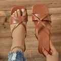 Detailansicht brauner flacher Sandalen mit Kreuzriemen und FASHION-Aufdruck. - Braun