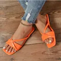 Detailaufnahme der leuchtend orangen flachen Sandalen mit Kreuzriemen. - Orange
