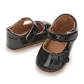 Close-up detail of black patent leather baby princess shoes with a sparkly bow accent - Black