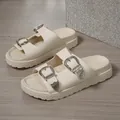Detailansicht von cremefarbenen Plateausandalen mit verzierten silbernen Schnallen. - Gebrochenes Weiß
