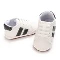 Close-up detail of white baby sneakers with soft sole and stylish black decorative stripes - White Black