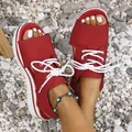 Detailed view of red platform peep-toe sandals with white laces on beach pebbles. - Red