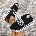 Close-up view of women's black platform sandals with white laces on a gravel background. - Black