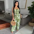 Ein trägerloser Jumpsuit mit grün-weißem Blattmuster in einer modernen Wohnzimmerumgebung. - S / Jumpsuits / Grün